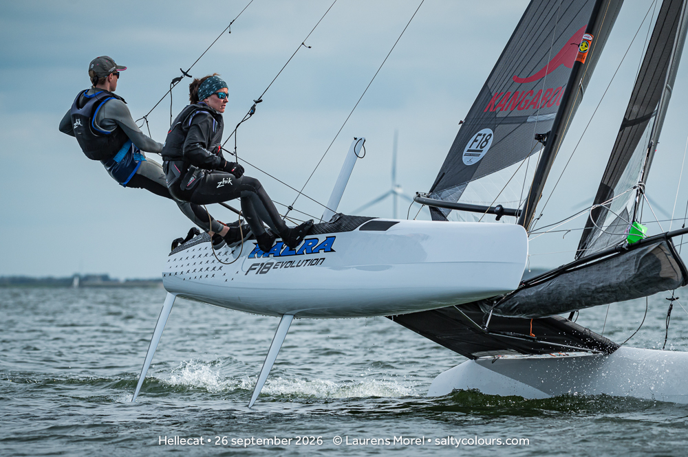 Formula-18-Katamaran am Wind, Steuermann und Vorschoterin im Doppeltrapez, dahinter ein Windrad