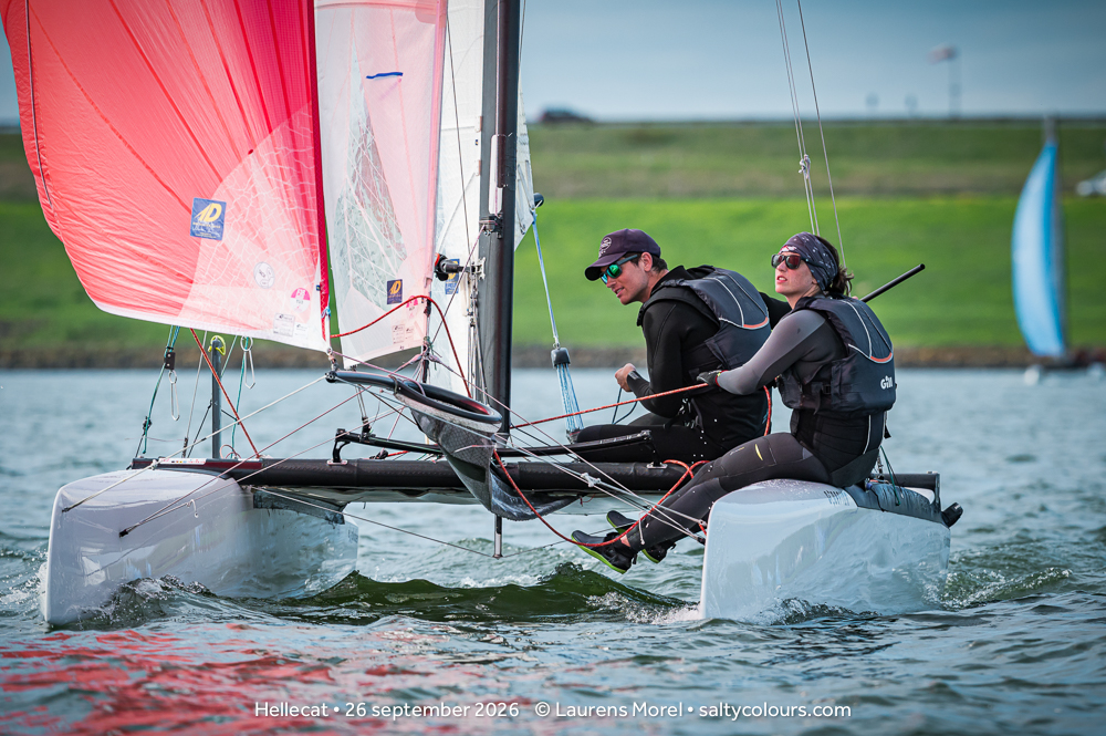 Formula-18-Crew unter rotem Gennaker bei leichtem Wind, dahinter der grüne Deich