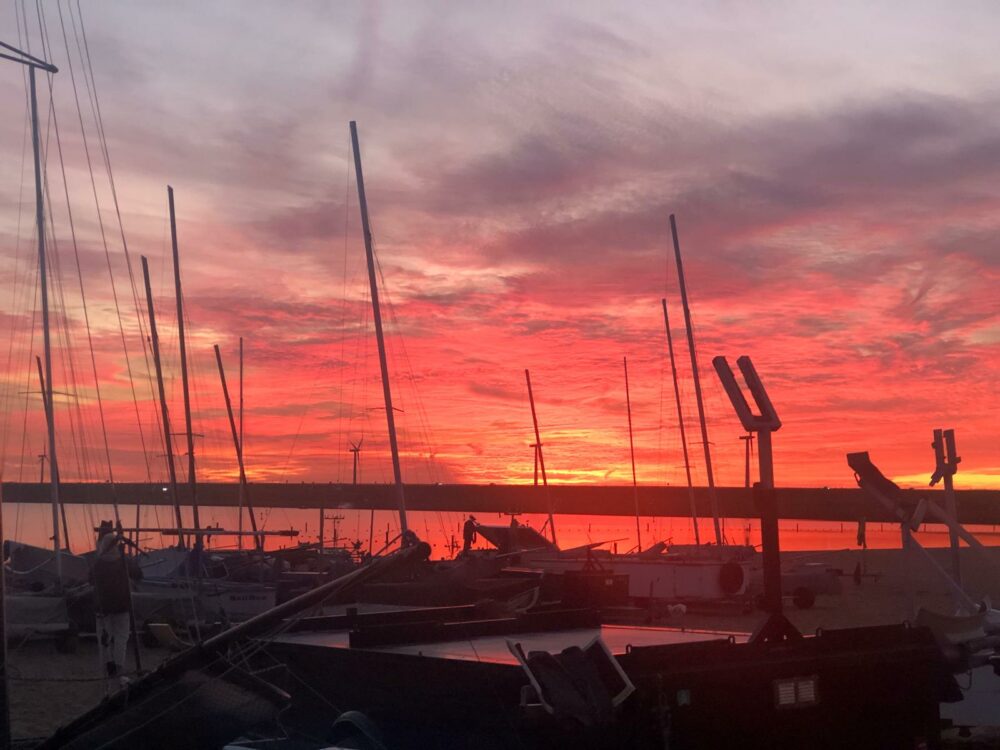 Masten der aufgebauten Katamarane vor tiefrotem Sonnenuntergang hinter dem Damm in Hellevoetsluis