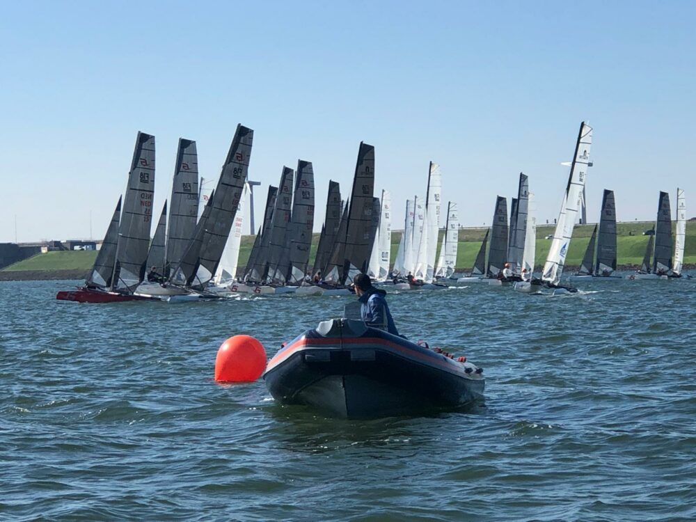 Formula-18-Flotte kurz nach dem Start, im Vordergrund Motorboot und orange Starttonne, dahinter der Deich